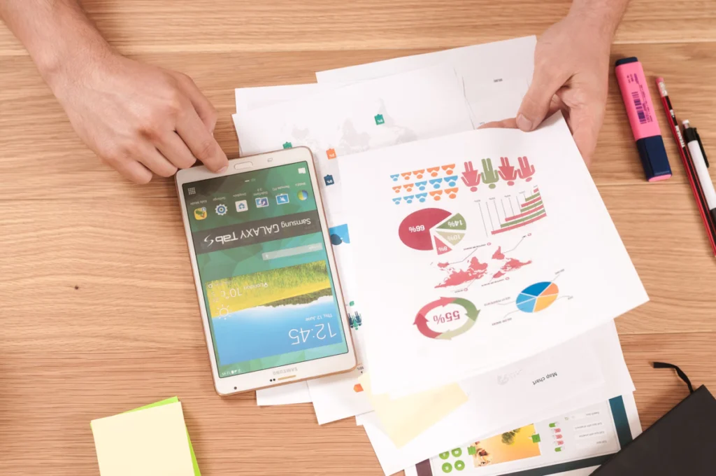 A person using a tablet and printed data sheets to forecast demand